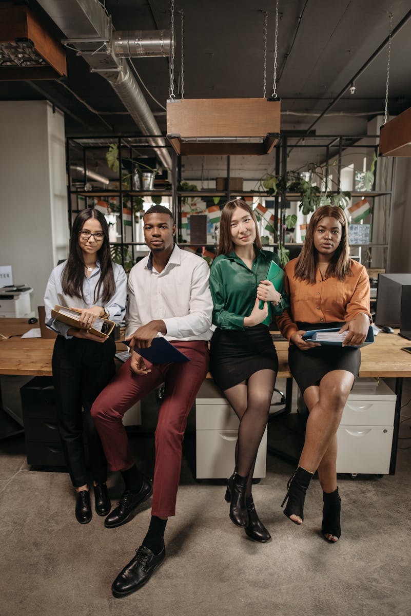 A diverse group of young professionals posing in a modern office setting, holding folders and looking confident.